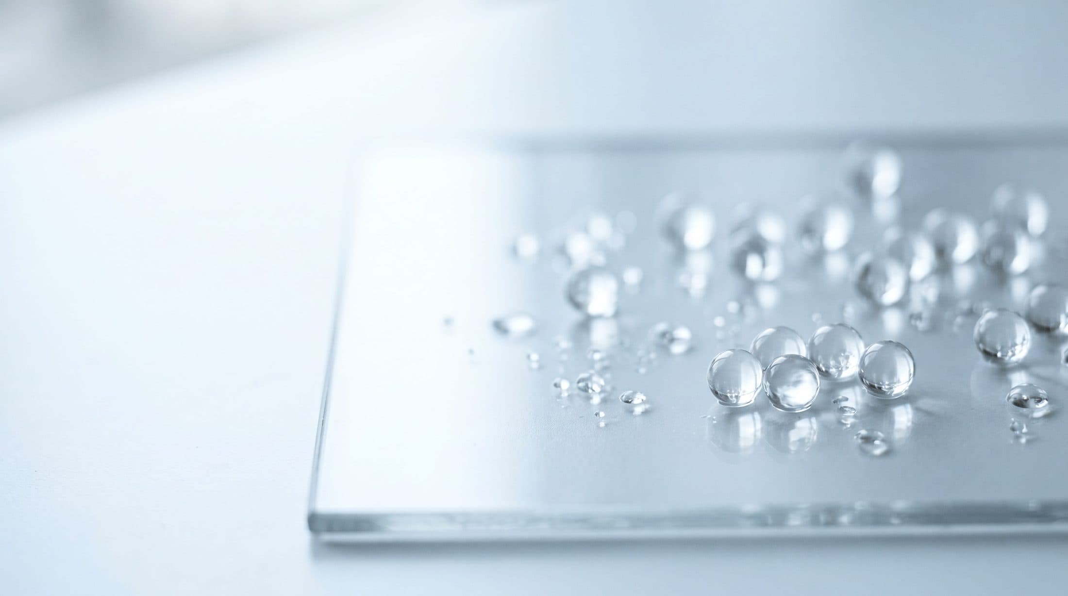 Klare Gel-Perlen und feine Tropfen auf einer hellen Glasfläche